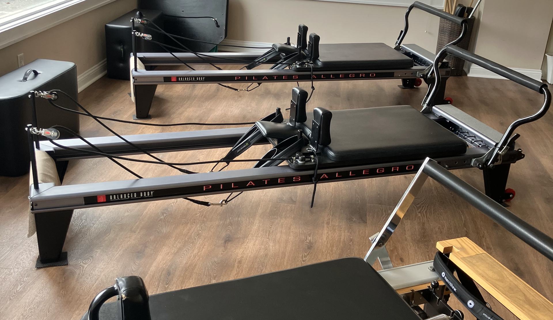 Black Allegro reformers on the wood floor at Essex Pilates & Wellness.