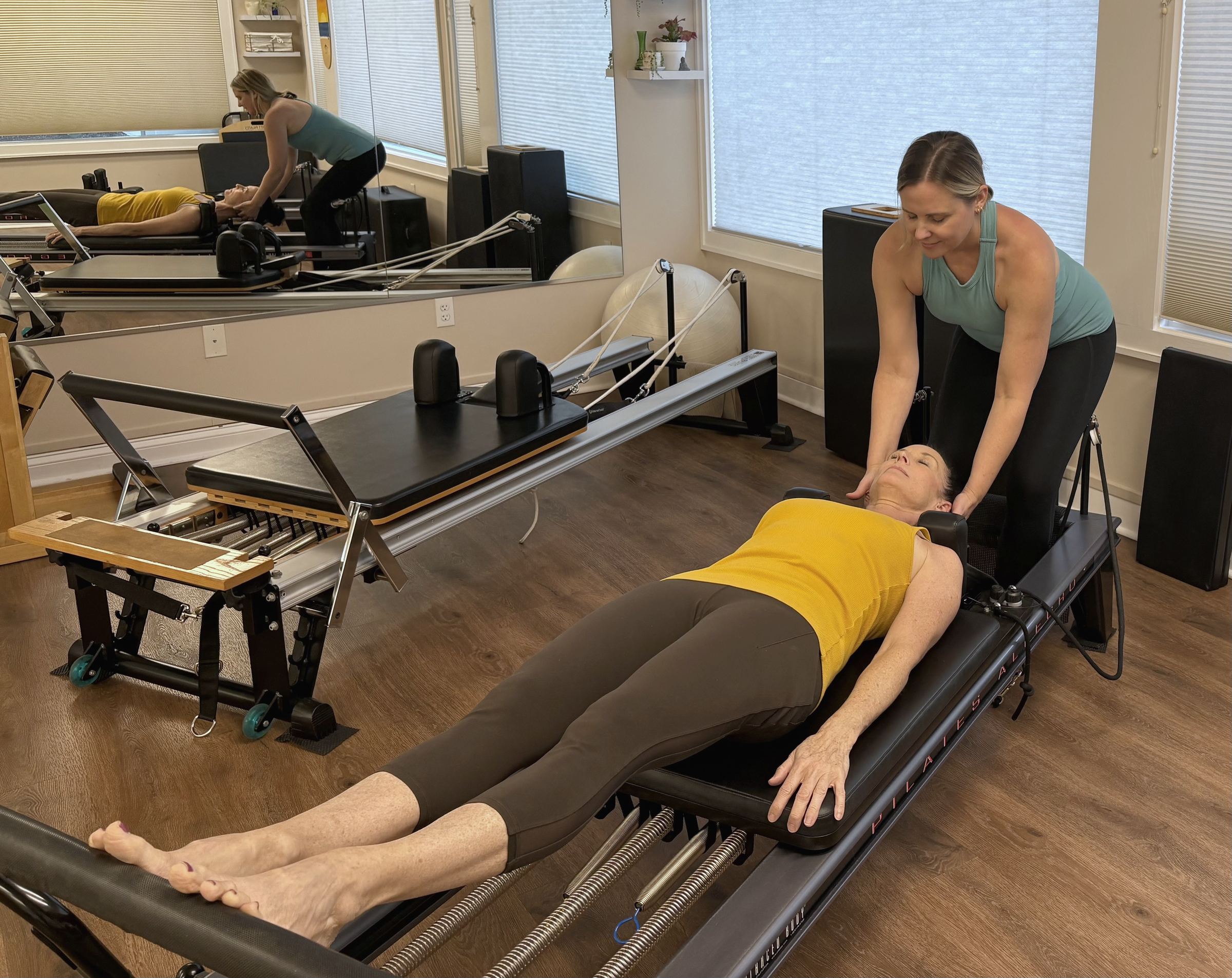 Nicole supporting a client's head and neck as she lies on a reformer.